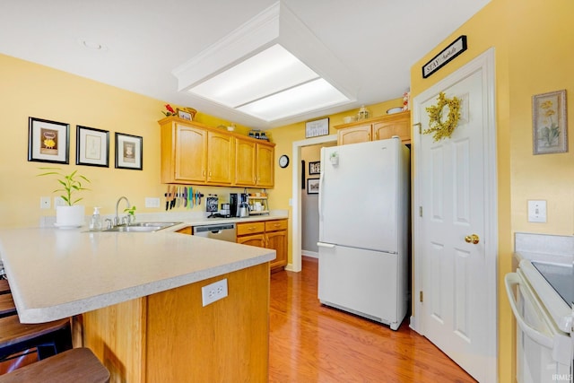 kitchen featuring light countertops, a kitchen bar, a peninsula, white appliances, and a sink