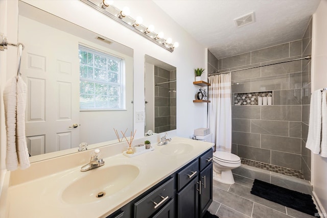 full bath featuring double vanity, visible vents, tiled shower, and a sink