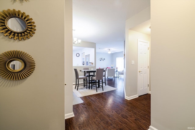 corridor featuring a notable chandelier, wood finished floors, and baseboards