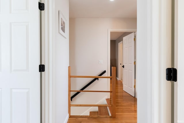 hall with an upstairs landing, light wood-type flooring, and baseboards