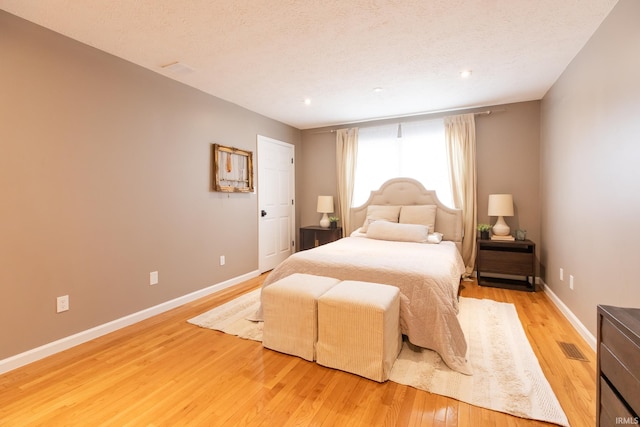 bedroom featuring light wood finished floors, a textured ceiling, and baseboards