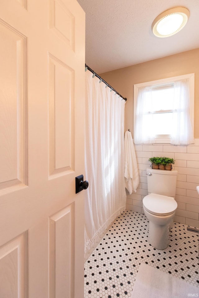 bathroom with tile patterned floors, toilet, curtained shower, a textured ceiling, and tile walls