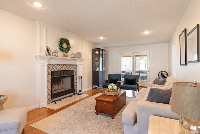 living room with a textured ceiling, recessed lighting, light wood finished floors, baseboards, and a tile fireplace