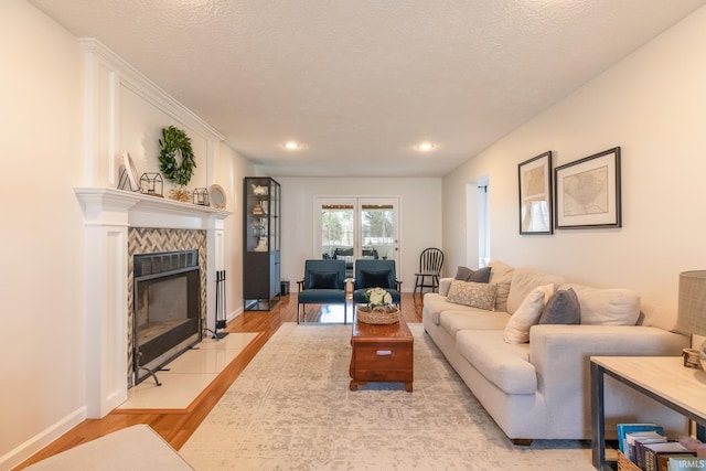 living room with a tiled fireplace, baseboards, light wood-type flooring, and a textured ceiling