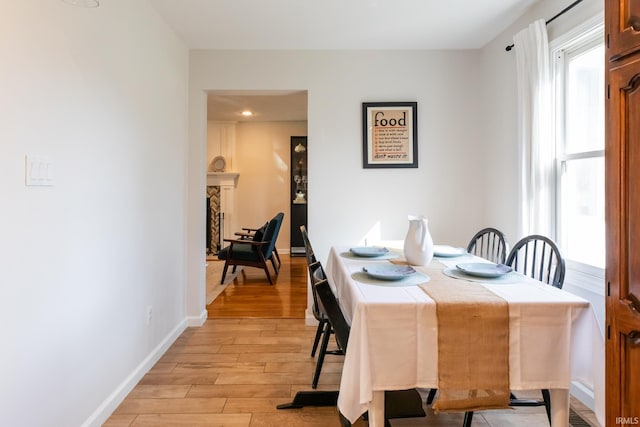 dining room featuring baseboards, light wood-style floors, and a fireplace