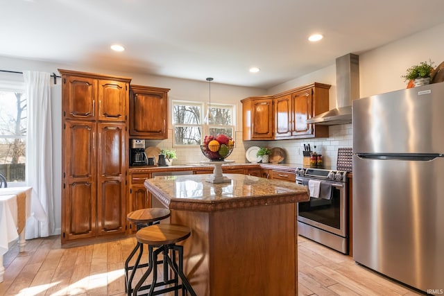 kitchen with tasteful backsplash, a center island, stainless steel appliances, wall chimney exhaust hood, and light wood finished floors