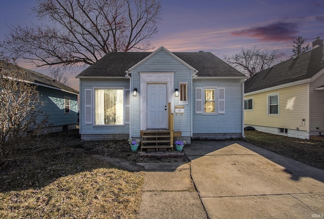 bungalow-style home with entry steps, driveway, and roof with shingles