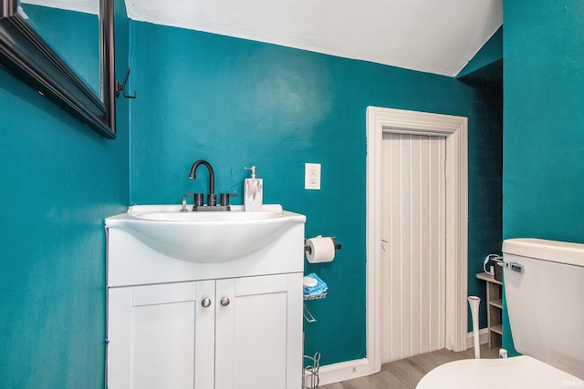 half bathroom featuring toilet, vanity, baseboards, and wood finished floors