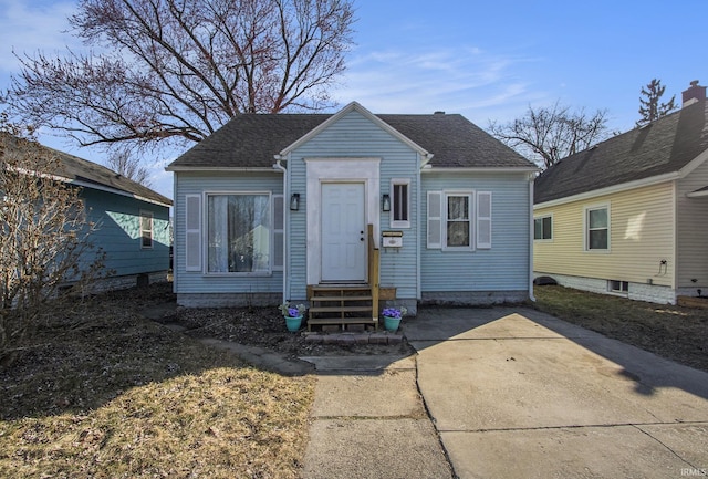 bungalow with a shingled roof, concrete driveway, and entry steps