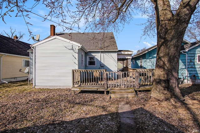 back of house with a deck, roof with shingles, and a chimney