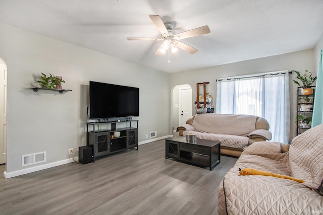 living area with baseboards, wood finished floors, arched walkways, and ceiling fan