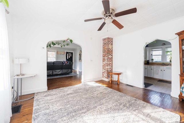 living area with visible vents, dark wood-style floors, arched walkways, and ceiling fan