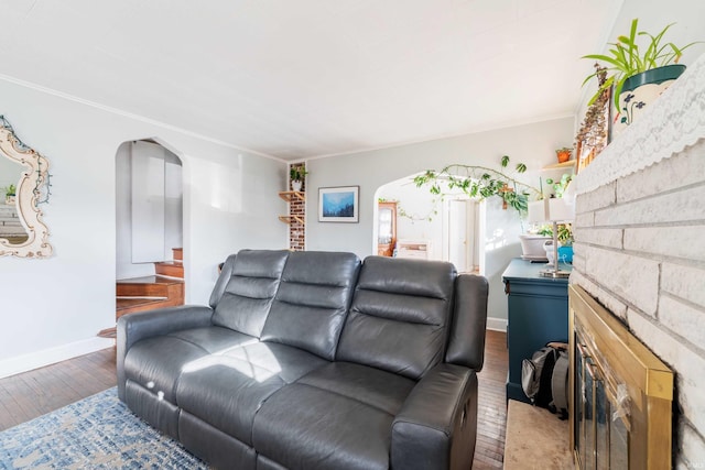 living area featuring crown molding, baseboards, a fireplace, hardwood / wood-style flooring, and arched walkways