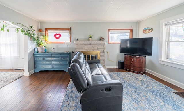 living area with dark wood-style floors, a glass covered fireplace, baseboards, and ornamental molding