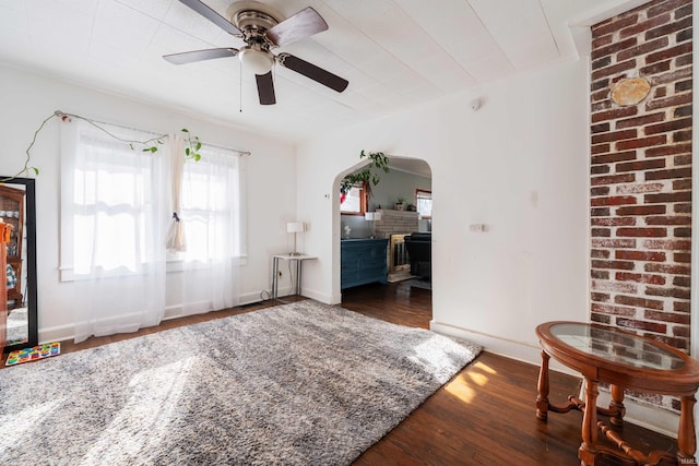 interior space featuring baseboards, wood finished floors, arched walkways, and ceiling fan