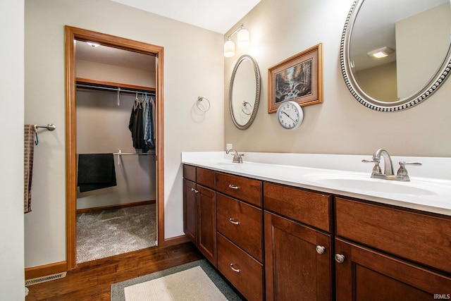 bathroom with wood finished floors, visible vents, double vanity, a sink, and a walk in closet