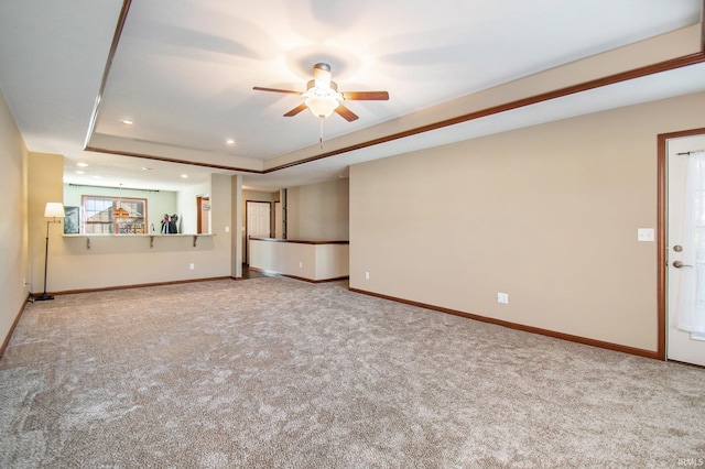 unfurnished living room with a tray ceiling, carpet floors, baseboards, and ceiling fan