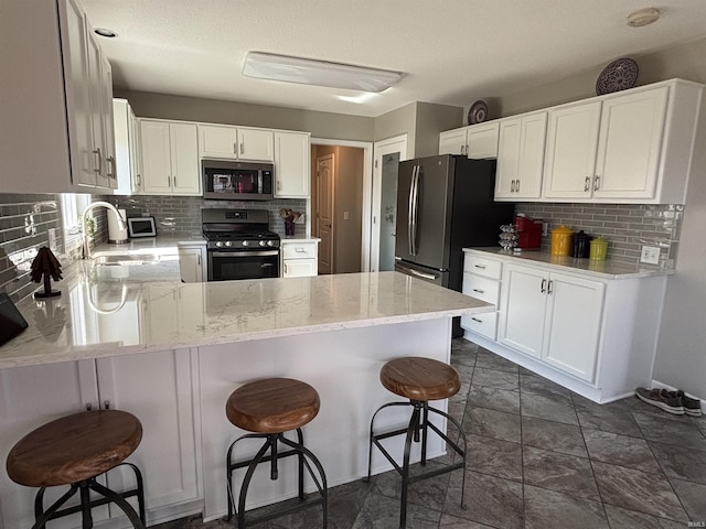 kitchen featuring backsplash, appliances with stainless steel finishes, a peninsula, and a sink