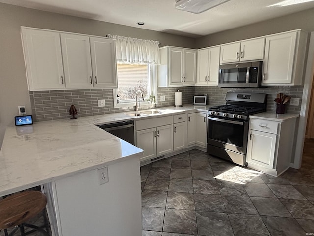 kitchen featuring a peninsula, a sink, decorative backsplash, stainless steel appliances, and white cabinetry