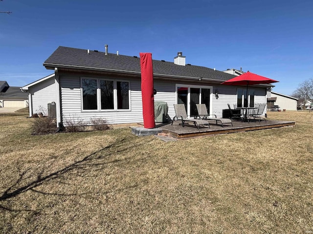 back of property with a shingled roof, a wooden deck, cooling unit, a chimney, and a yard