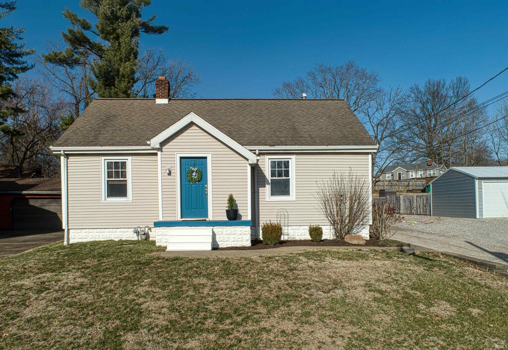 view of front of home with fence, roof with shingles, a chimney, a front lawn, and an outdoor structure