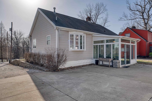 rear view of property with a patio area, roof with shingles, a chimney, and a sunroom