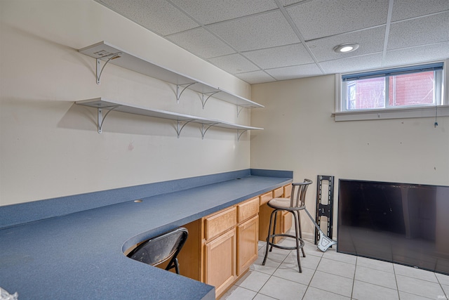 unfurnished office featuring a paneled ceiling, light tile patterned flooring, and built in study area