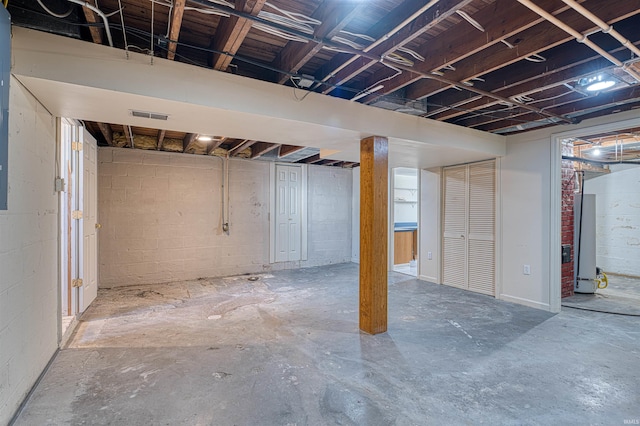 unfinished basement with visible vents, concrete block wall, and water heater