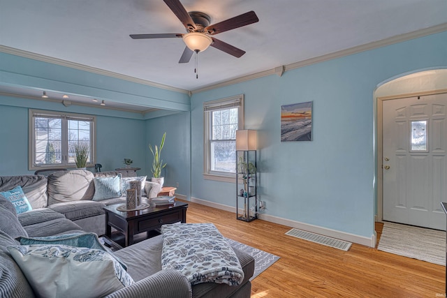 living area with light wood-style flooring, a ceiling fan, visible vents, and ornamental molding