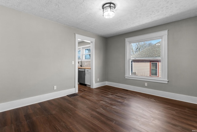 unfurnished room with visible vents, dark wood-type flooring, a sink, a textured ceiling, and baseboards