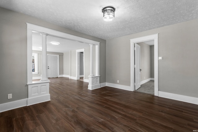 empty room featuring a textured ceiling, baseboards, dark wood-type flooring, and ornate columns