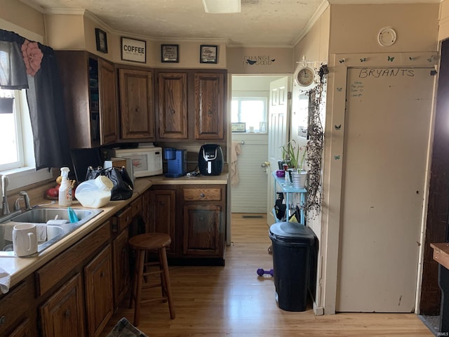 kitchen featuring white microwave, a sink, light countertops, light wood-style floors, and crown molding