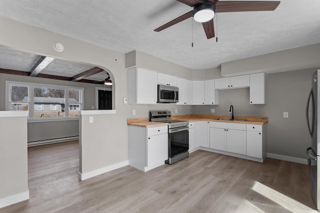 kitchen with ceiling fan, baseboard heating, arched walkways, stainless steel appliances, and a sink