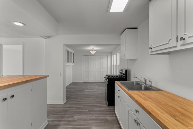 kitchen with dark wood-style floors, stainless steel range with gas stovetop, a sink, white cabinets, and butcher block counters