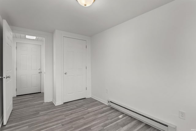 unfurnished bedroom with wood finished floors, baseboards, and a baseboard radiator