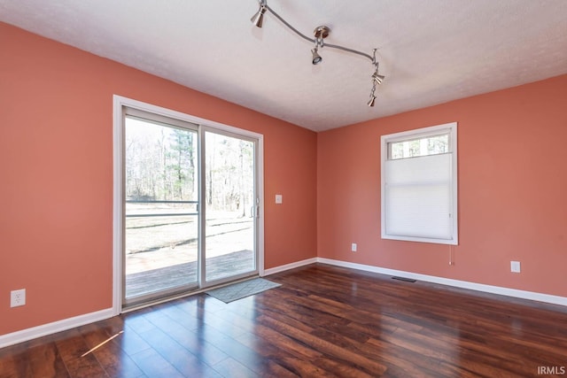 unfurnished room featuring dark wood finished floors, plenty of natural light, and baseboards