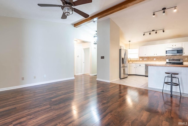 unfurnished living room with baseboards, ceiling fan, lofted ceiling with beams, wood finished floors, and a sink