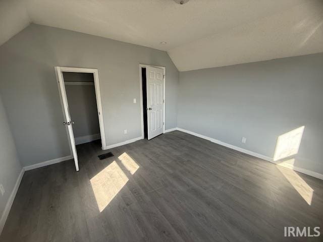 unfurnished bedroom with visible vents, baseboards, dark wood-type flooring, and vaulted ceiling