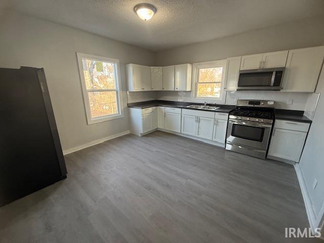 kitchen featuring a sink, stainless steel appliances, dark countertops, and white cabinetry