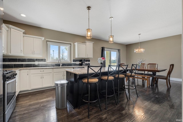 kitchen with stainless steel gas stove, a sink, a center island, white cabinetry, and dark wood-style flooring