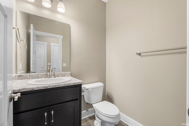 half bathroom featuring baseboards, toilet, and vanity