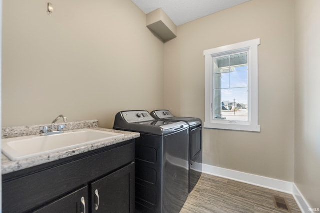 laundry room featuring a sink, dark wood-style floors, cabinet space, separate washer and dryer, and baseboards