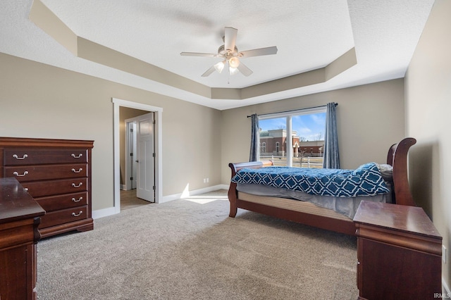 bedroom with baseboards, light colored carpet, a tray ceiling, a textured ceiling, and a ceiling fan