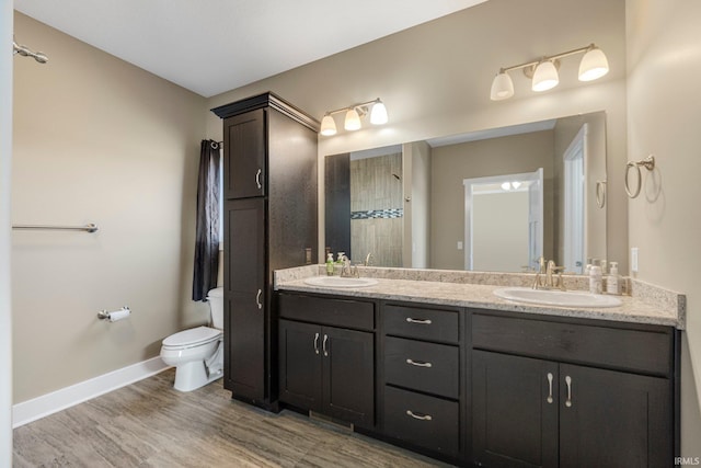 bathroom featuring baseboards, toilet, double vanity, wood finished floors, and a sink