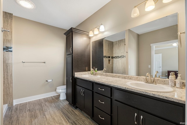 bathroom featuring double vanity, a tile shower, toilet, and a sink