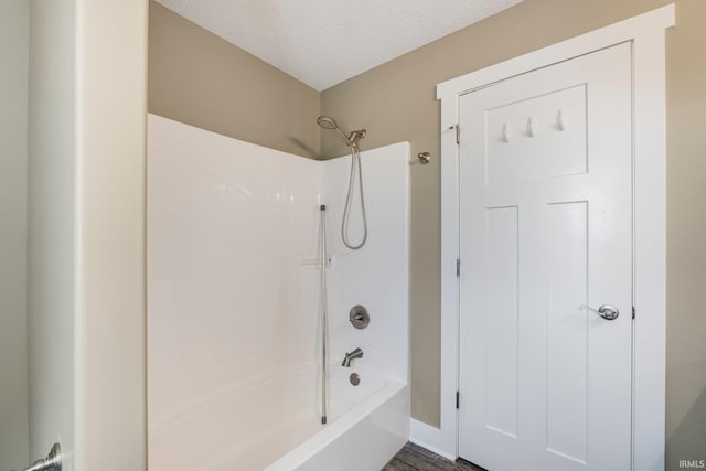 bathroom with a textured ceiling and shower / bathtub combination