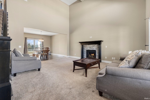 carpeted living room featuring baseboards, a stone fireplace, a towering ceiling, and an inviting chandelier