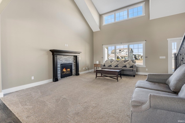 living area with baseboards, light carpet, a high ceiling, and a stone fireplace