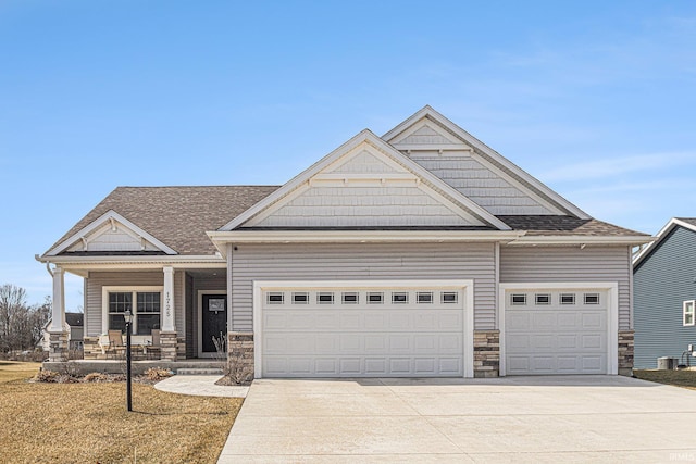 view of front of home featuring driveway, stone siding, roof with shingles, covered porch, and an attached garage