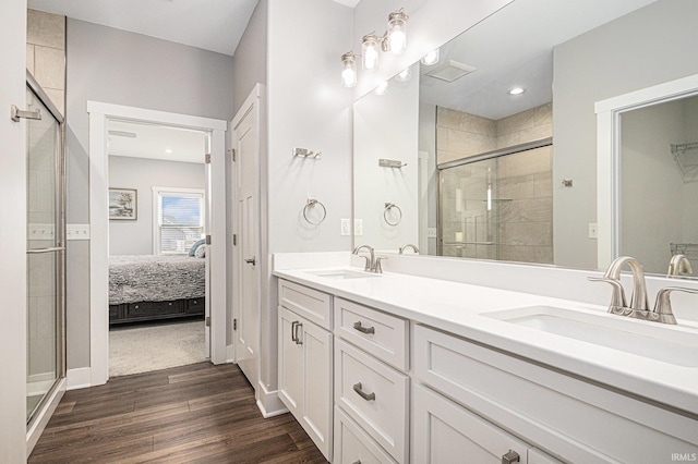 ensuite bathroom with double vanity, a shower stall, wood finished floors, and a sink